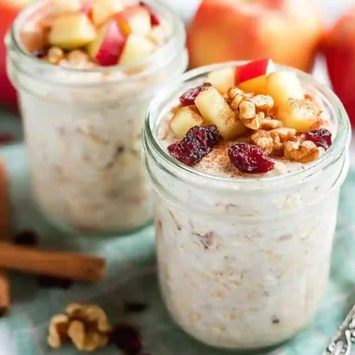 A glass jar filled with creamy apple cinnamon overnight oats, topped with diced apples, a sprinkle of cinnamon, and sometimes a dollop of yogurt, ready for a healthy breakfast.