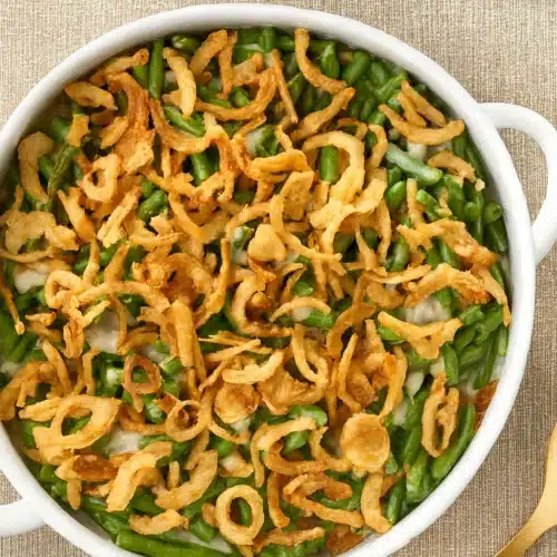 Classic green bean casserole topped with crispy fried onions in a white baking dish — creamy, crunchy, and easy Thanksgiving side dish.