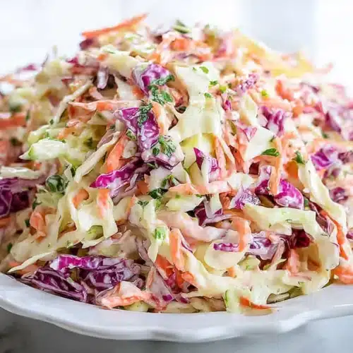 Colorful creamy coleslaw with green and purple cabbage, carrots, and fresh parsley served on a white plate.