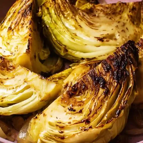 Golden roasted cabbage wedges with crispy edges, seasoned with herbs and garlic, on a white baking tray.