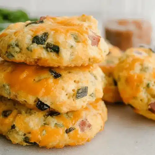 Close-up of savory, golden-brown Breakfast Protein Biscuits topped with melted cheese, ham, and green onions.