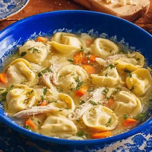 Two vibrant cobalt blue bowls of a hearty Chicken Tortellini Soup Recipe, garnished with fresh herbs and Parmesan, on a rustic wooden table.