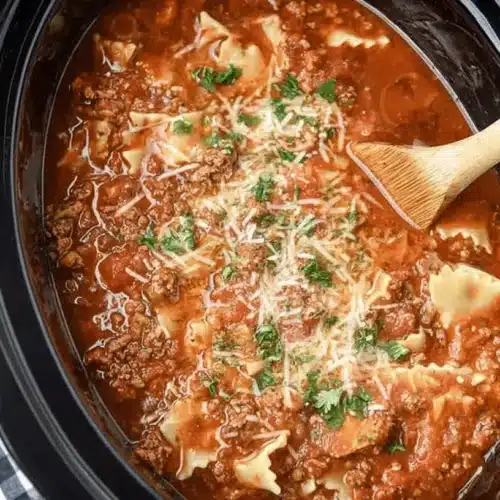 A close-up overhead view of a hearty Crockpot Lasagna Soup in a slow cooker, garnished with melted cheese and fresh parsley, served with toasted bread.