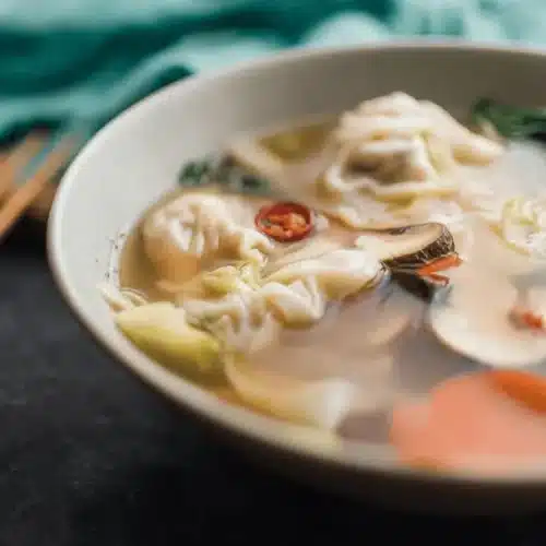 Steaming bowl of Asian wonton soup with dumplings, vegetables, and mushrooms, a perfect example of hearty soup recipes.
