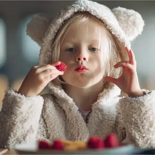 A young child delightedly eats fresh berries, showcasing healthy and delicious Sugar-Free Candy Alternatives.