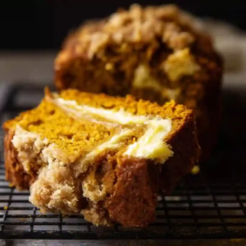 Moist chocolate loaf cake sliced on a board, with one slice on a plate and two coffee cups nearby.