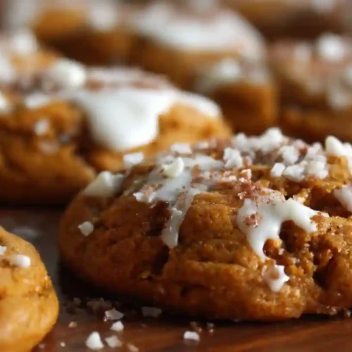 Soft, chewy pumpkin cookies topped with a drizzle of white icing and crunchy sugar on a baking board.
