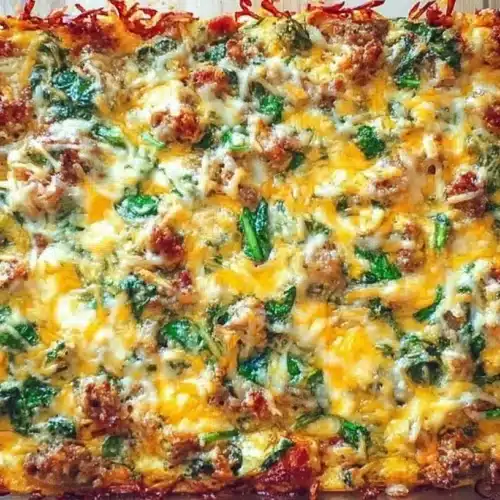 Overhead view of a delicious Cheesy Sausage Breakfast Casserole with melted cheese, crumbled sausage, and spinach in a glass baking dish.
