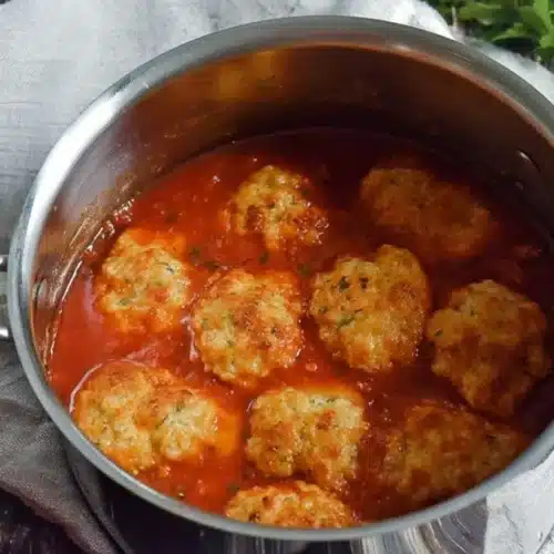 A stainless steel pot brimming with vibrant Hearty Tomato Soup and golden-brown Cheddar Bay Dumplings, garnished with fresh herbs on a rustic wooden surface.