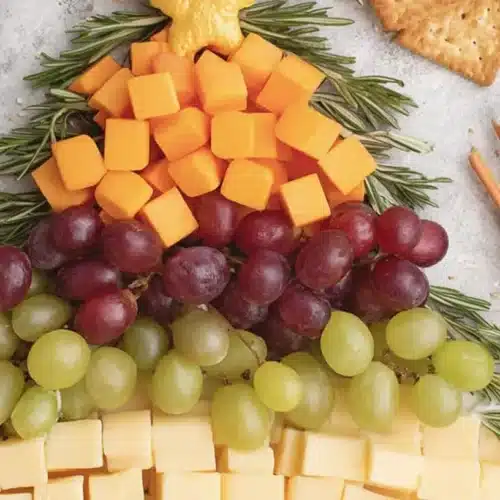 A festive Christmas tree-shaped charcuterie board featuring cheese, grapes, and rosemary, ideal for Christmas party food ideas appetizers.