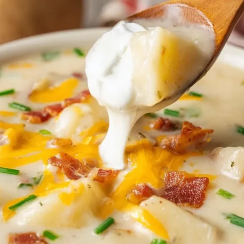 Close-up of a steaming bowl of Comforting Loaded Baked Potato Soup, generously topped with melted cheddar, crispy bacon, and fresh chives, with a spoon adding sour cream.