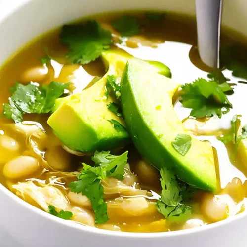 Close-up of a hearty bowl of Easy White Chicken Chili, garnished with fresh avocado and cilantro on a white background.