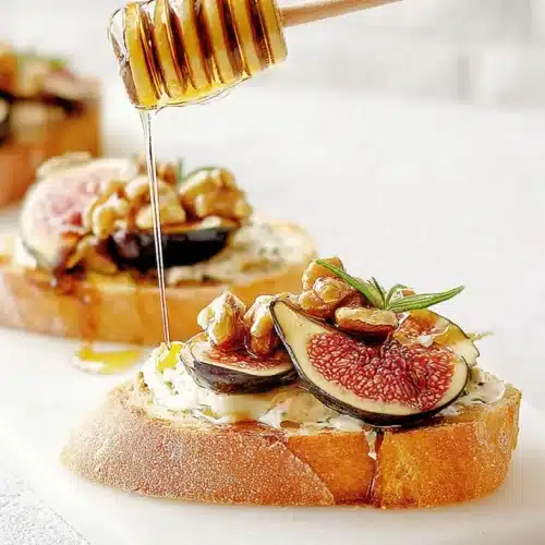 Elegant finger foods: Gourmet fig and walnut crostini drizzled with golden honey on a white board.