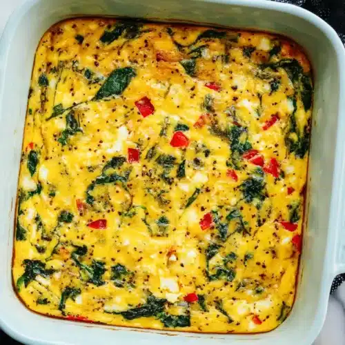 Overhead view of a vibrant Healthy Breakfast Casserole with spinach, red bell pepper, and feta in a blue baking dish.
