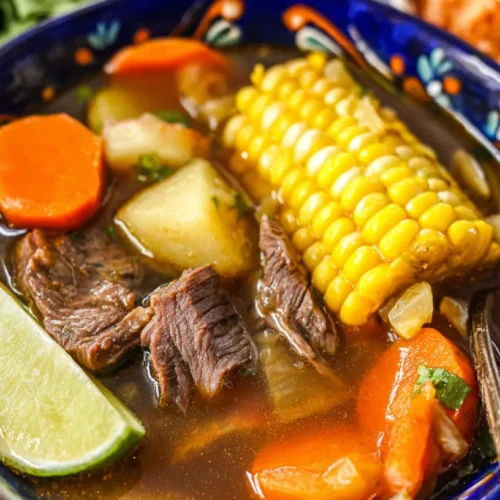 Vibrant Mexican Beef Soup (caldo de res) in a hand-painted ceramic bowl with corn, carrots, potatoes, and a fresh lime wedge.
