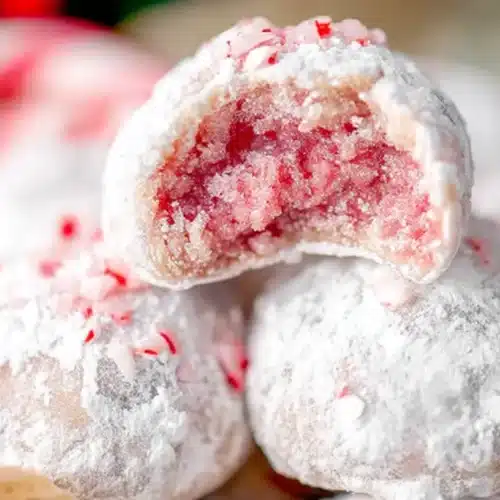 Close-up of festive Peppermint Snowball Cookies, with one broken to reveal its pink interior and red peppermint flecks.