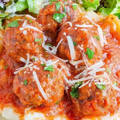 Hearty Porcupine Meatballs with rich tomato sauce, creamy mashed potatoes, and a fresh side salad, garnished with cheese and herbs.
