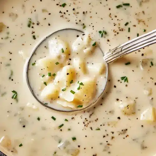 Overhead view of a creamy, hearty serving of The Best Potato Soup in a blue Dutch oven with a ladle and fresh chives.