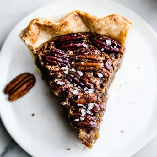 An overhead shot of a delicious slice of The Maple Pecan Pie with a flaky crust and toasted pecans on a white plate.